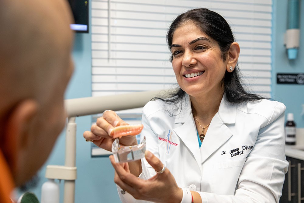 Dr. Uttma Dham showing a denture model to a patient